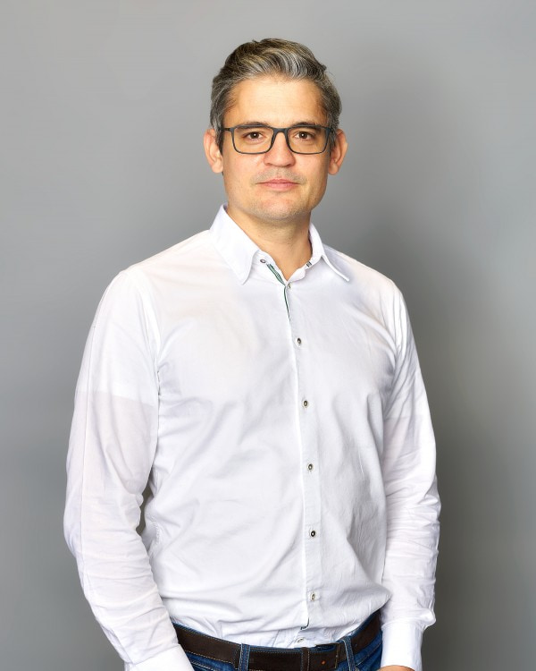 Dr. Stephan Zellner; -	Der zweite von den beiden Geschäftsführern trägt auch ein weißes Hemd, eine Brille und hat die Haare nach hinten gestylt.